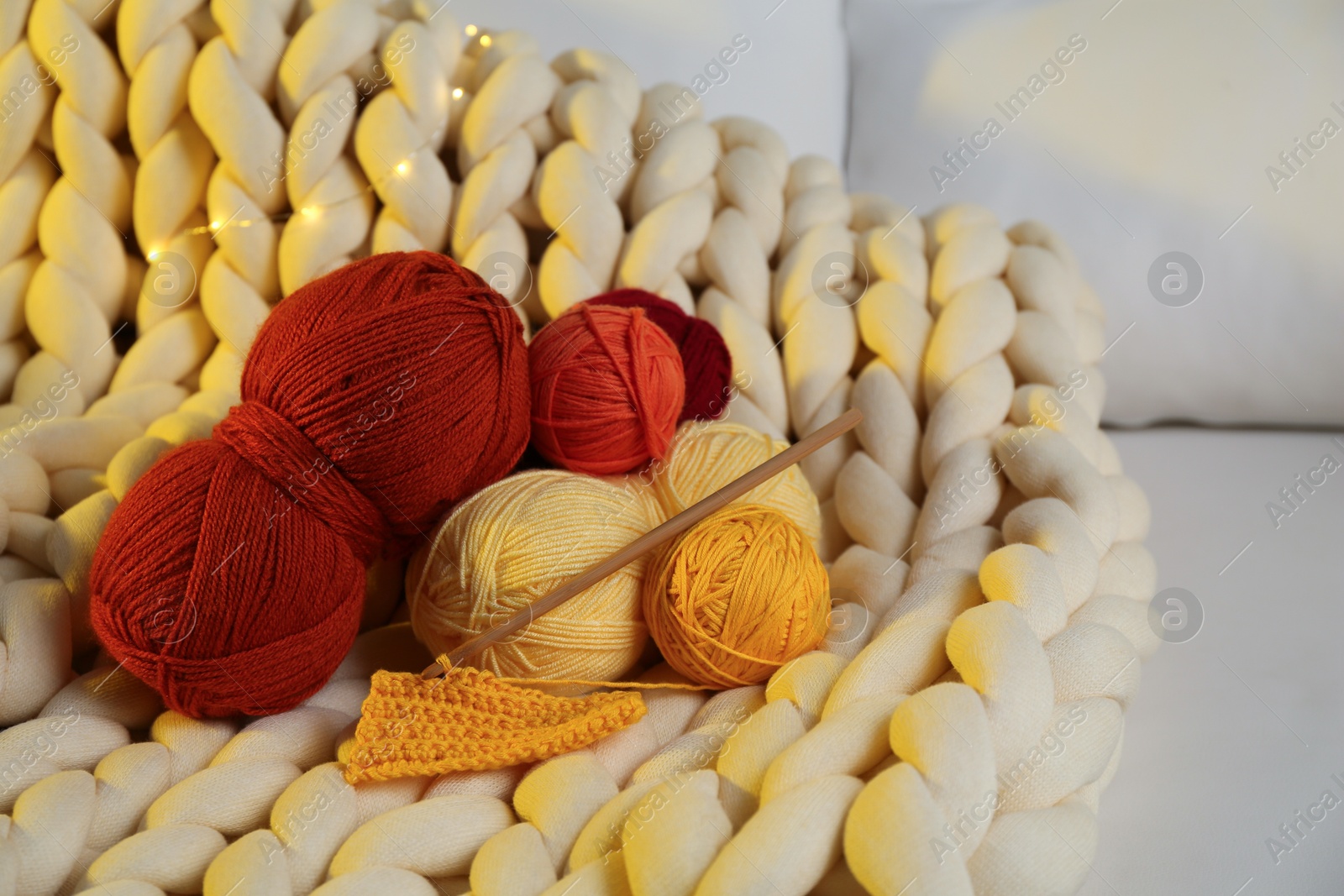 Photo of Colorful yarns, crochet pattern, hook and festive lights on blanket