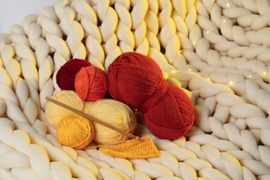 Photo of Colorful yarns, crochet pattern, hook and festive lights on blanket