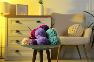 Photo of Colorful yarns and knitting needles on coffee table in cozy room