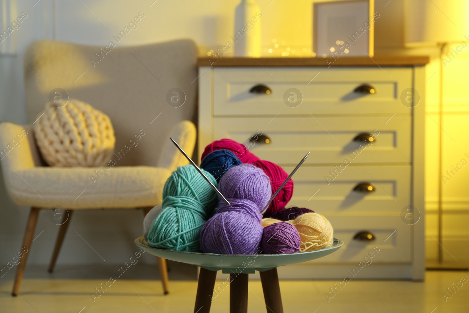 Photo of Colorful yarns and knitting needles on coffee table in cozy room