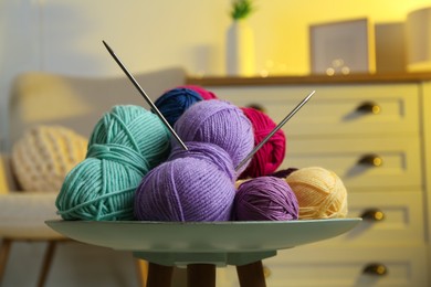 Photo of Colorful yarns and knitting needles on coffee table in cozy room