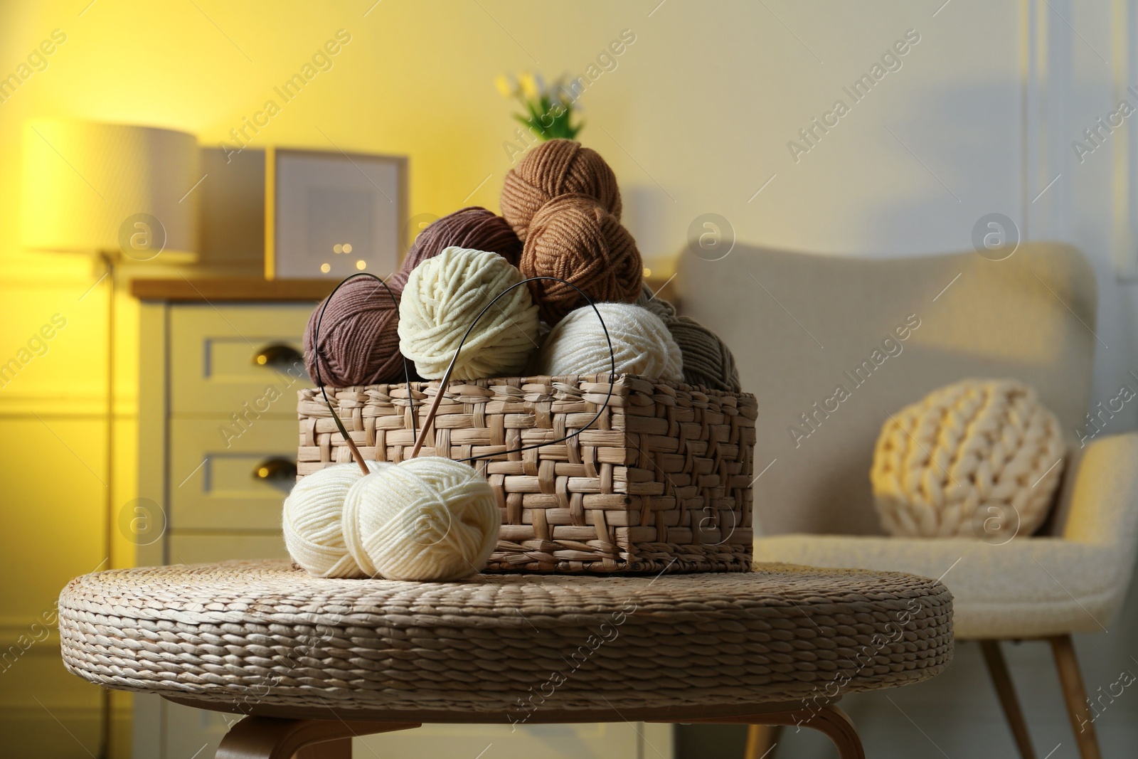 Photo of Wicker basket with colorful yarns and knitting needles on coffee table in cozy room