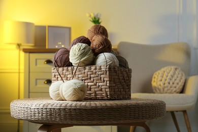 Photo of Wicker basket with colorful yarns and knitting needles on coffee table in cozy room