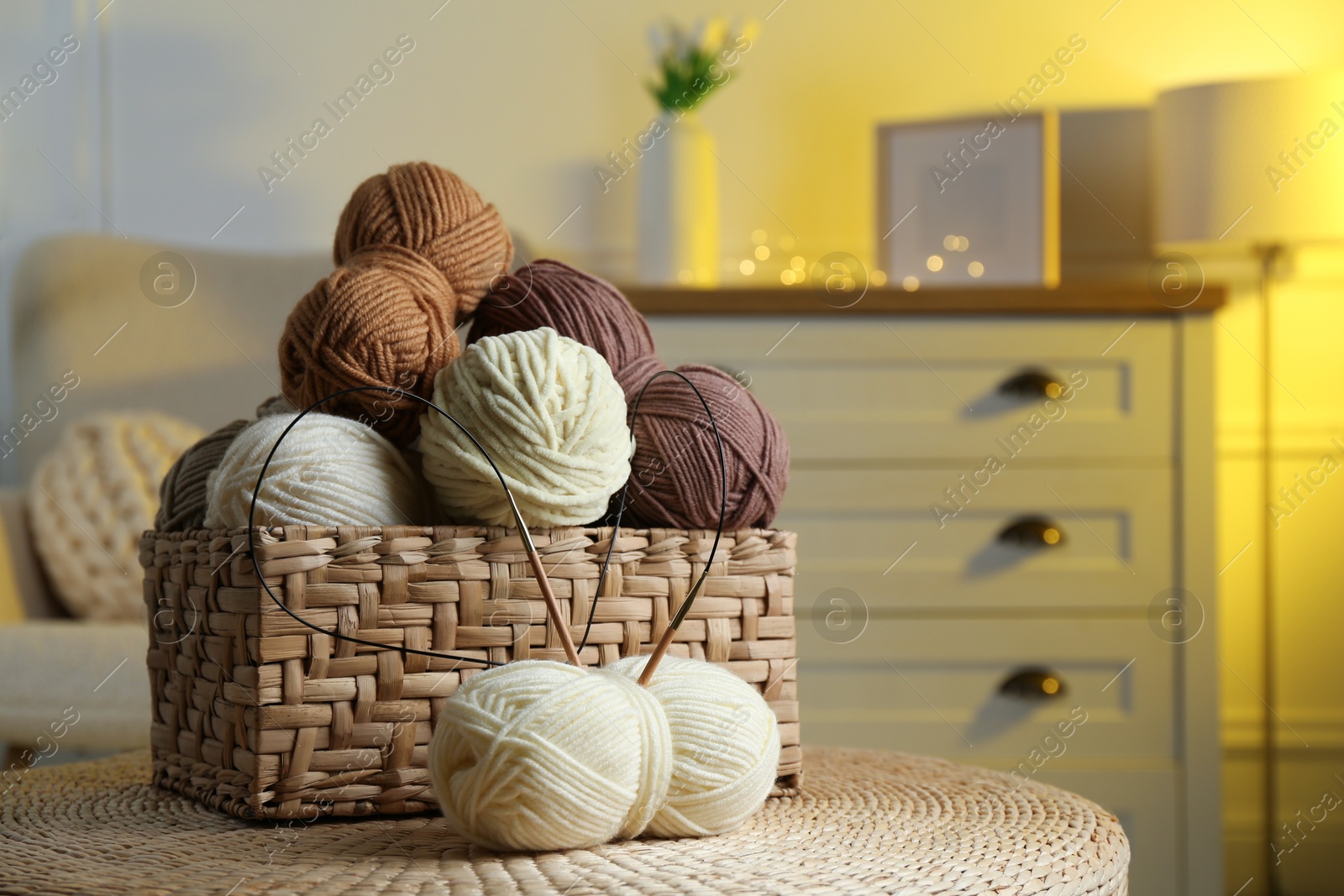 Photo of Wicker basket with colorful yarns and knitting needles on coffee table in cozy room