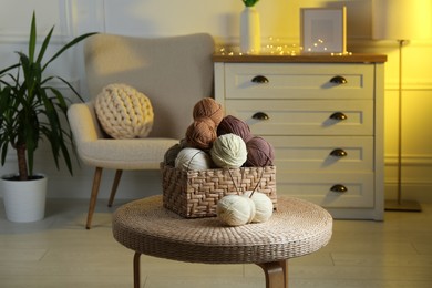 Photo of Wicker basket with colorful yarns and knitting needles on coffee table in cozy room