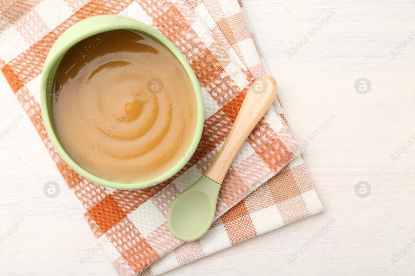 Photo of Delicious baby food in bowl and spoon on white wooden table, flat lay