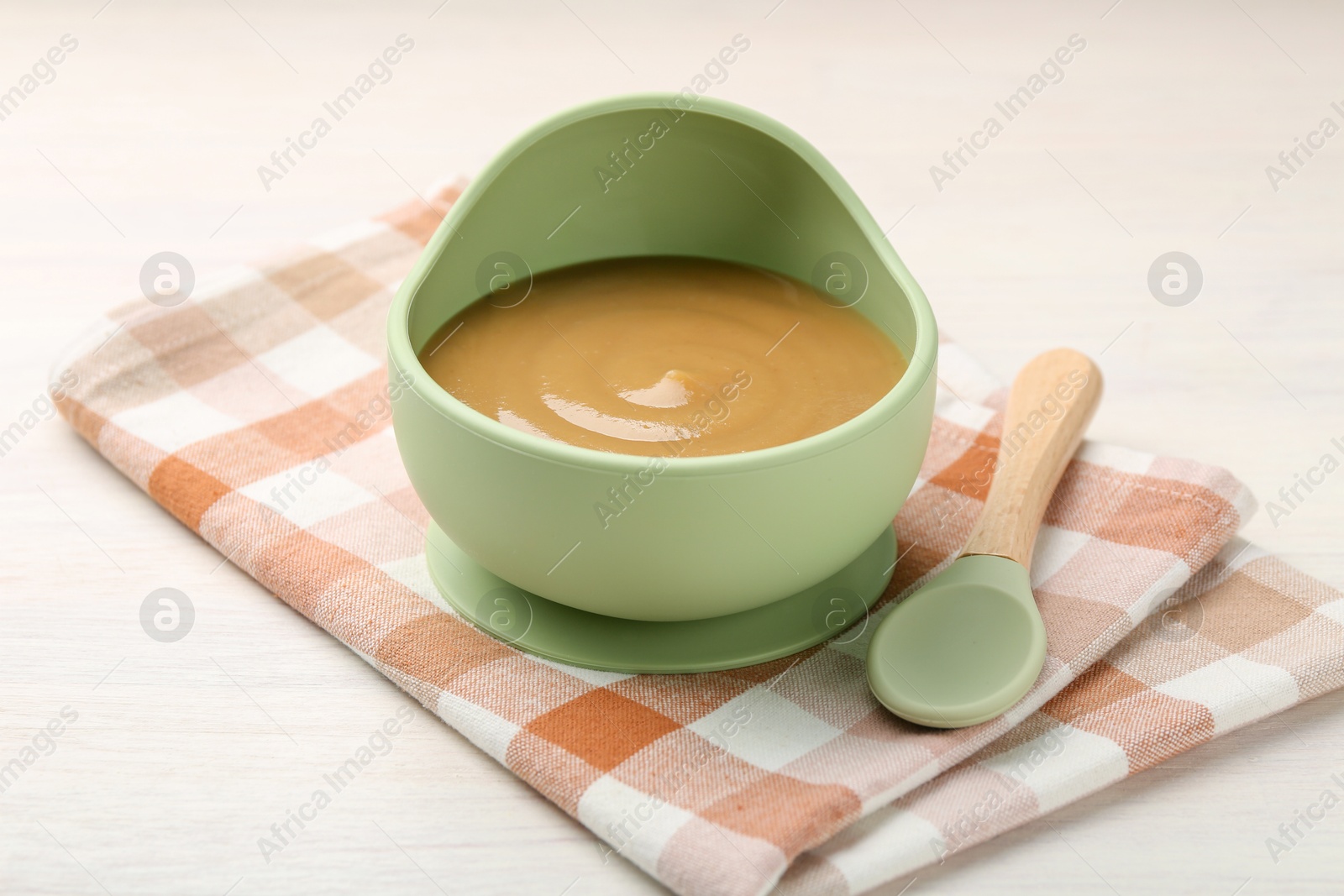 Photo of Delicious baby food in bowl and spoon on white wooden table