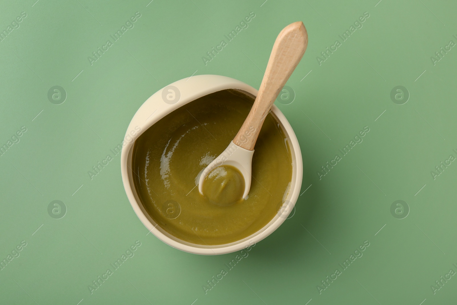 Photo of Delicious baby food with spoon in bowl on green table, top view