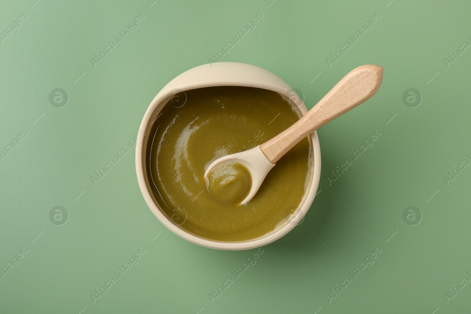 Photo of Delicious baby food with spoon in bowl on green table, top view