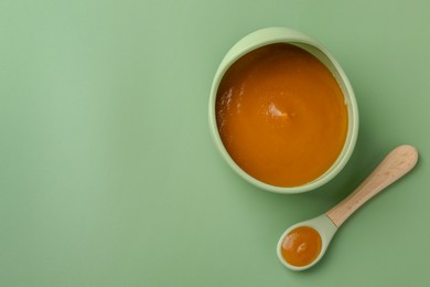 Photo of Delicious baby food in bowl with spoon on green table, flat lay. Space for text