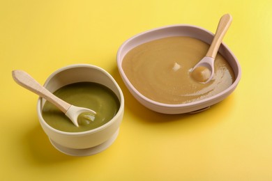 Photo of Delicious baby food and spoons in bowls on yellow table