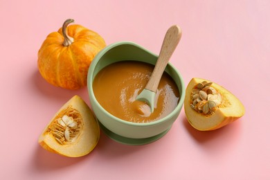 Photo of Delicious baby food with spoon in bowl and fresh pumpkins on pink table