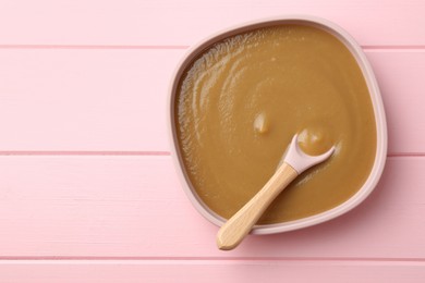 Photo of Delicious baby food and spoon in bowl on pink wooden table, top view. Space for text