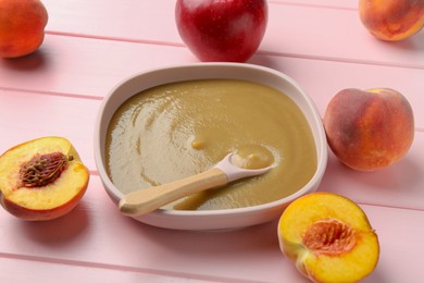 Photo of Delicious baby food with spoon in bowl and fresh ingredients on pink wooden table