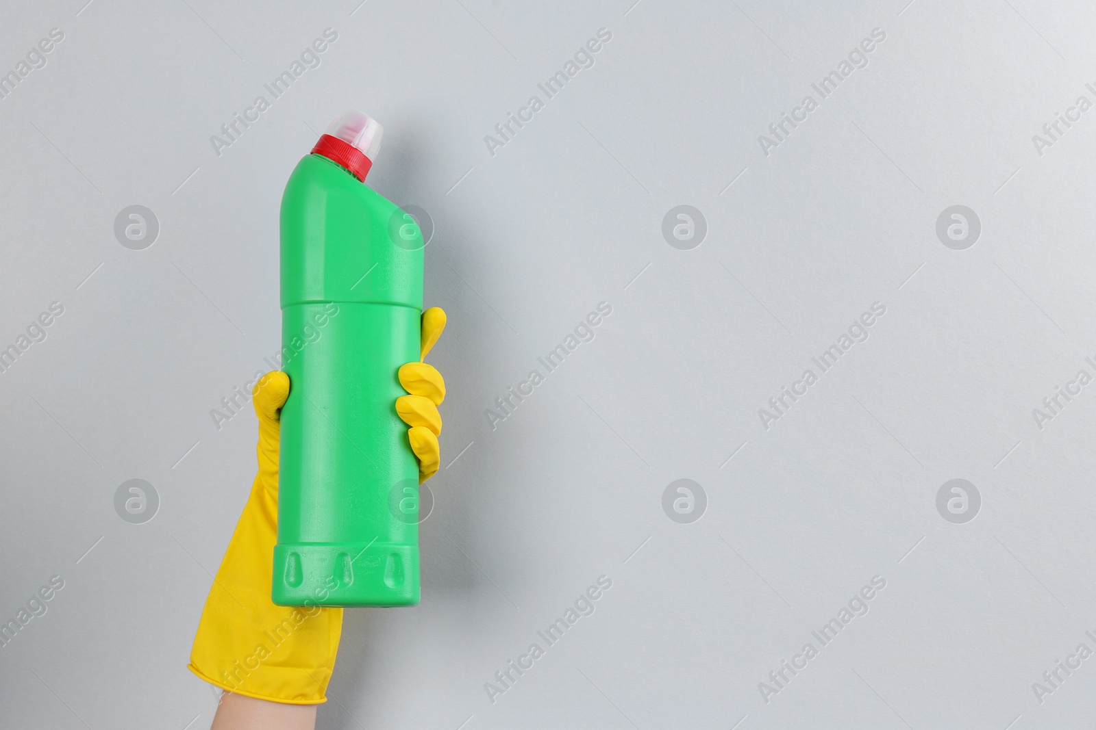 Photo of Woman holding toilet cleaner in bottle on light background, closeup. Space for text