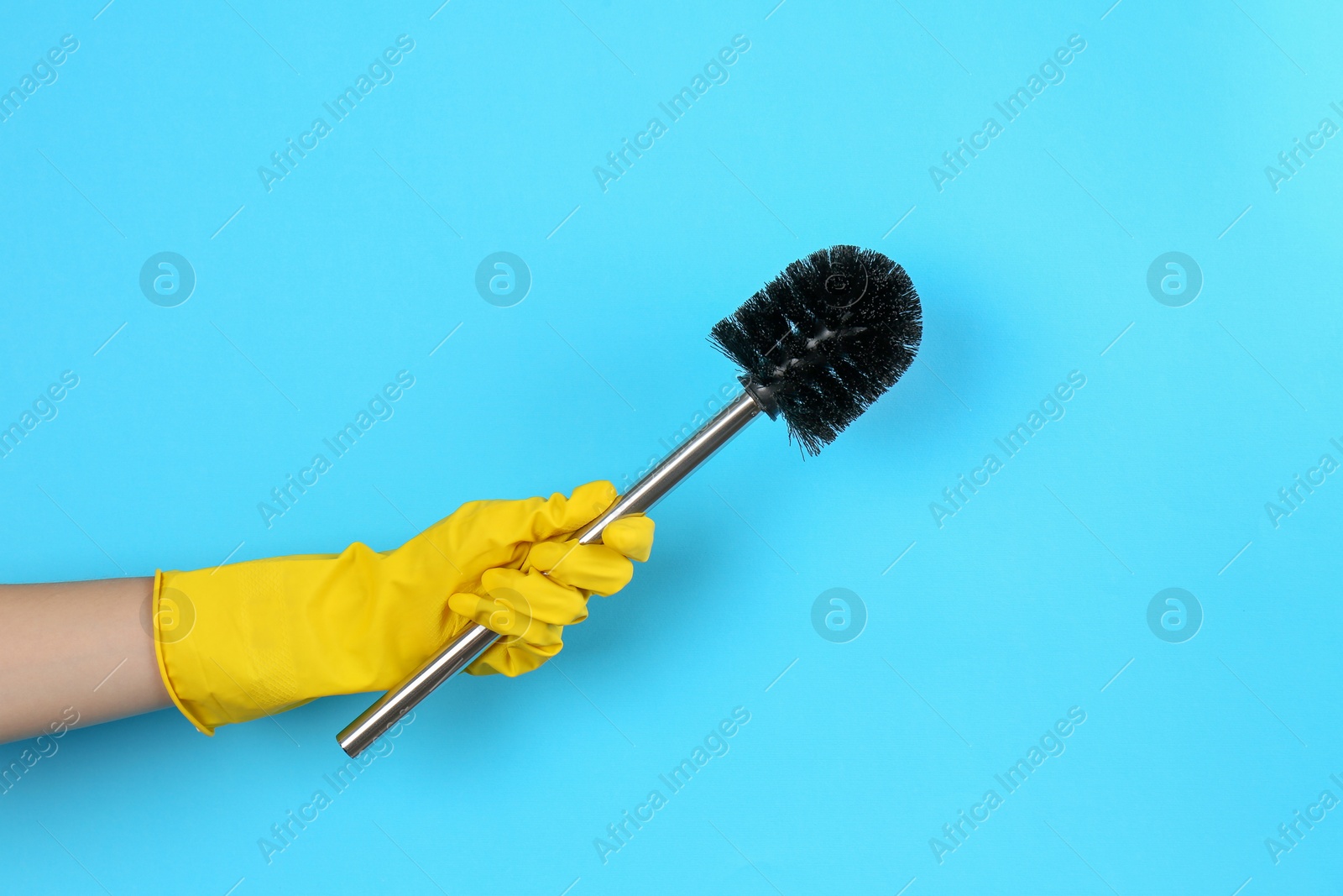 Photo of Woman holding black toilet brush on light blue background, closeup. Cleaning tool