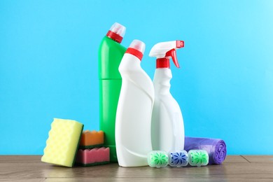 Photo of Different toilet cleaners, sponges and trash bags on wooden table against light blue background