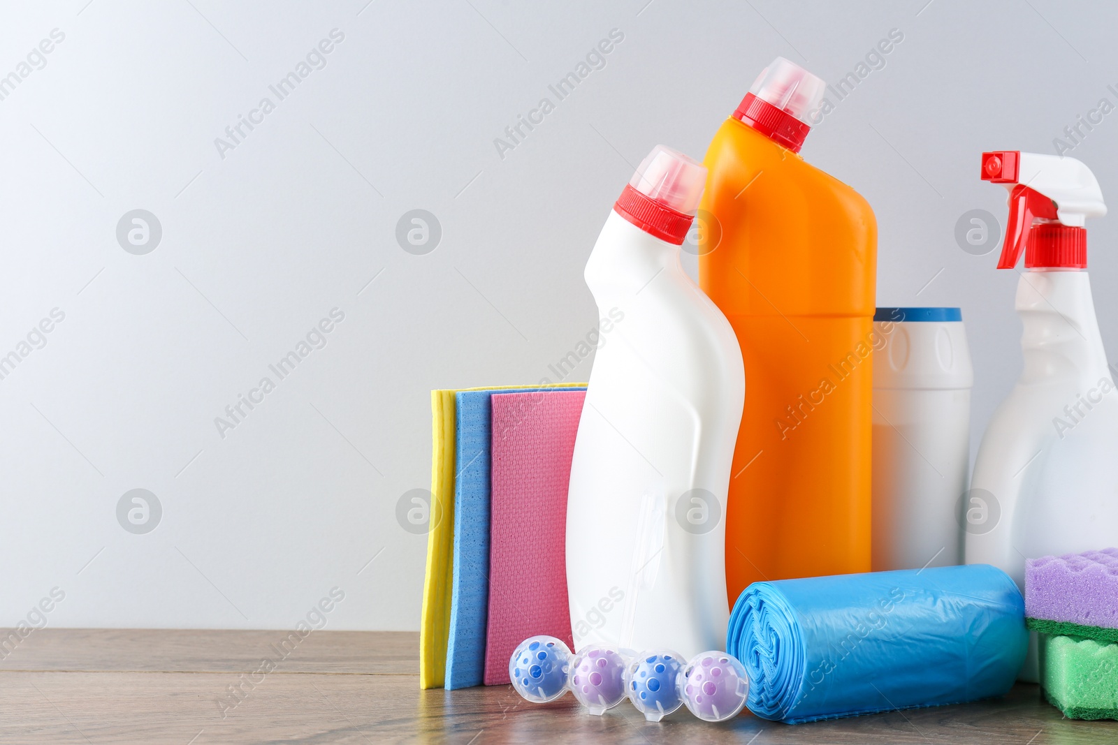 Photo of Different toilet cleaners, sponges and trash bags on wooden table against light grey background. Space for text