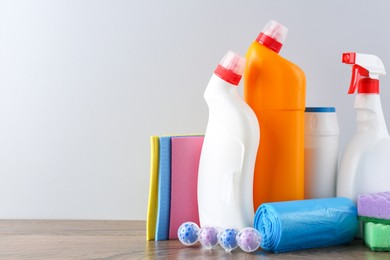 Photo of Different toilet cleaners, sponges and trash bags on wooden table against light grey background. Space for text