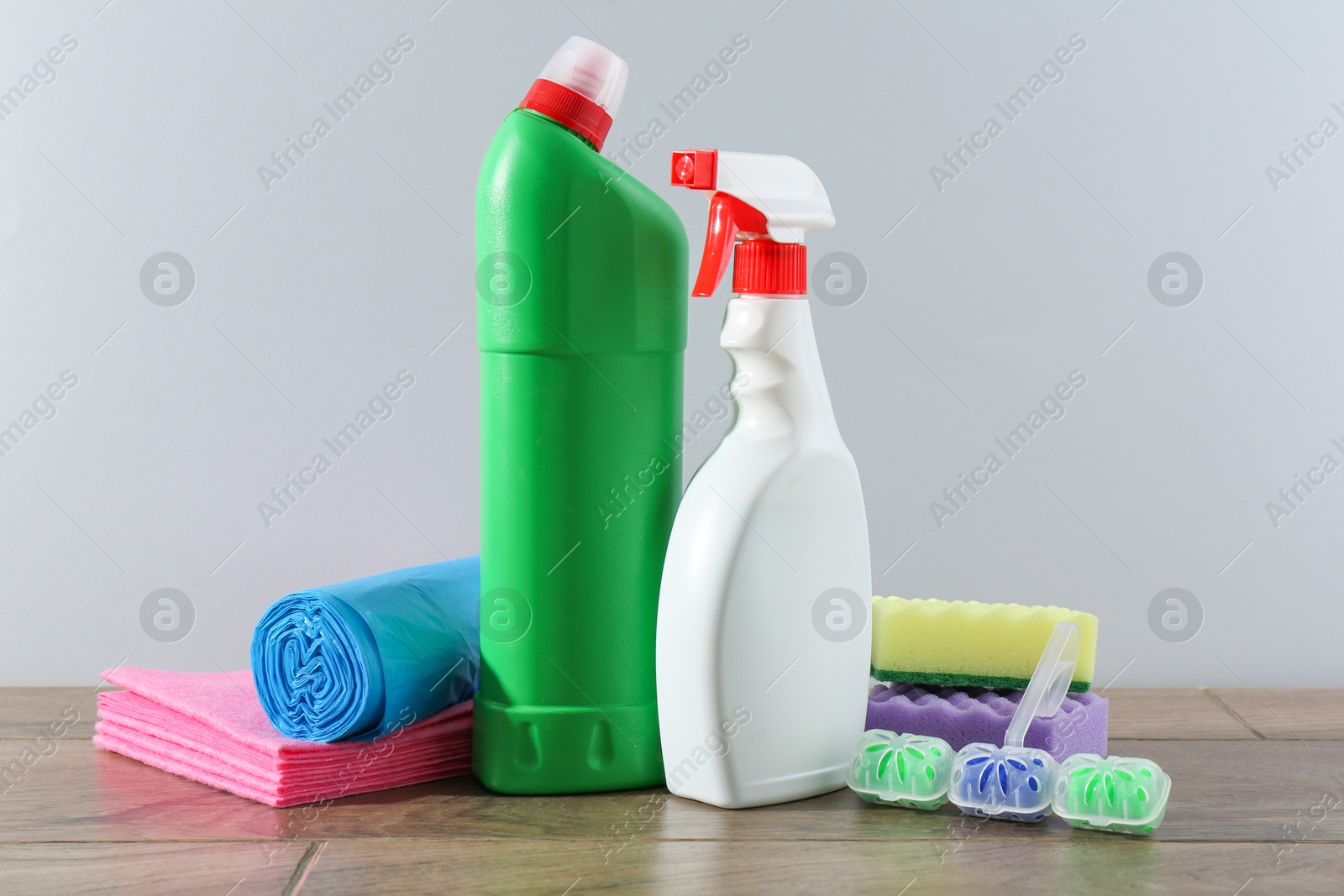 Photo of Different toilet cleaners, sponges and trash bags on wooden table against light grey background