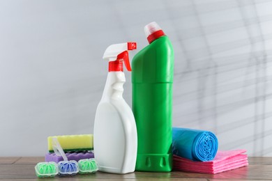 Photo of Different toilet cleaners, sponges and trash bags on wooden table against light grey background