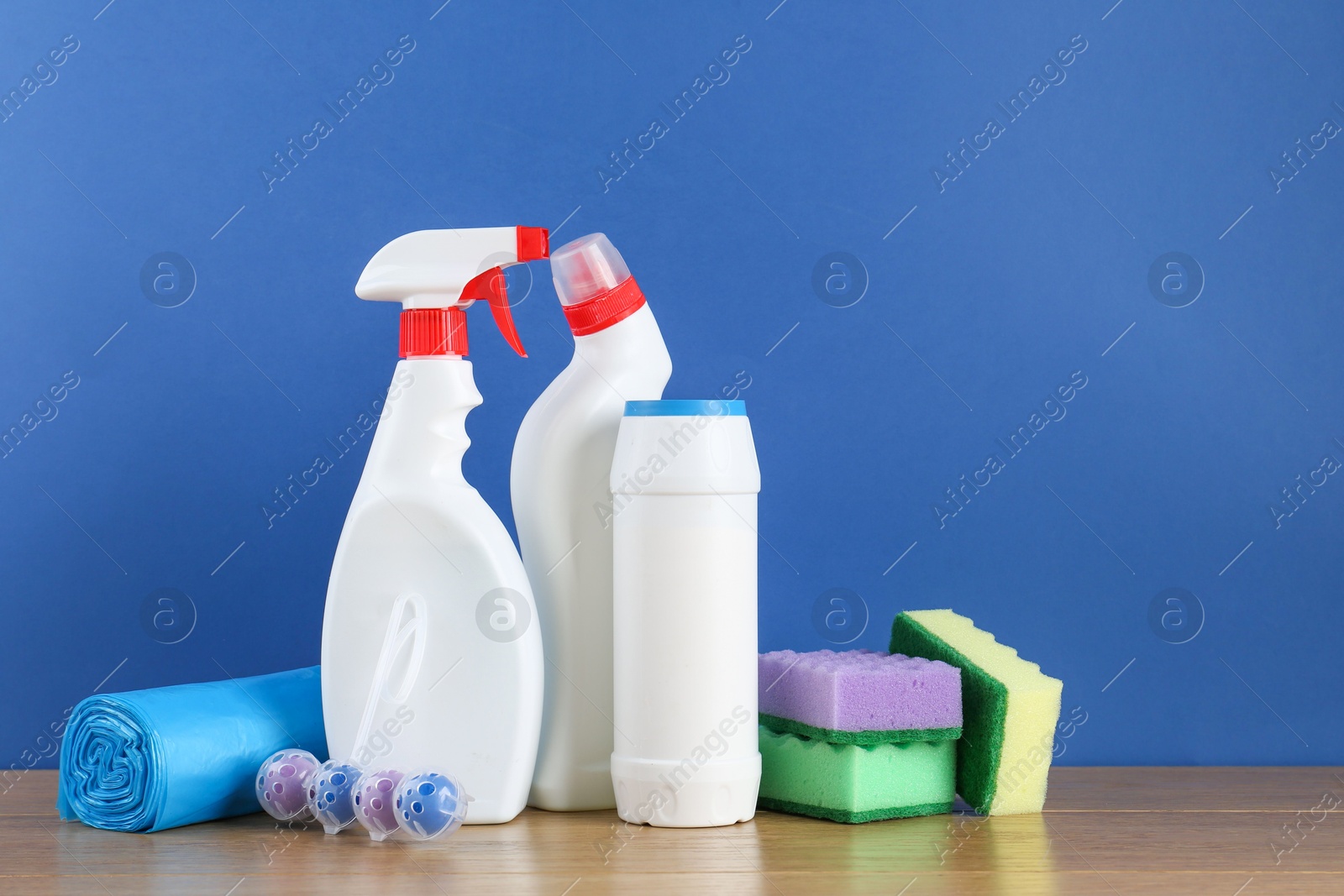 Photo of Different toilet cleaners, sponges and trash bags on wooden table against blue background. Space for text