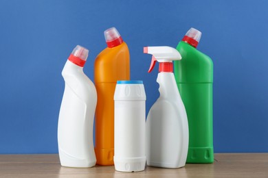 Photo of Different toilet cleaners on wooden table against blue background