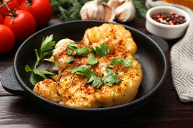 Photo of Tasty cauliflower steak in frying pan and other products on wooden table, closeup