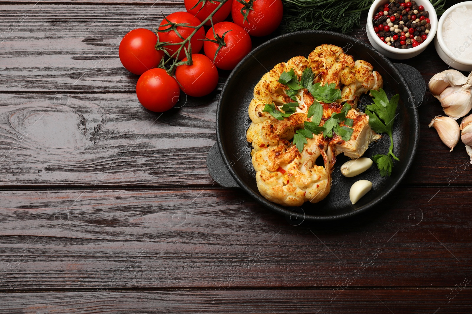 Photo of Tasty cauliflower steak in frying pan and other products on wooden table, top view. Space for text