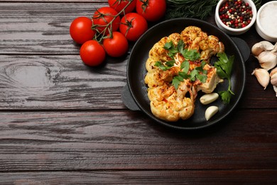 Photo of Tasty cauliflower steak in frying pan and other products on wooden table, top view. Space for text