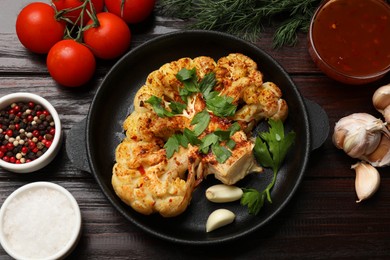 Photo of Tasty cauliflower steak in frying pan and other products on wooden table, top view