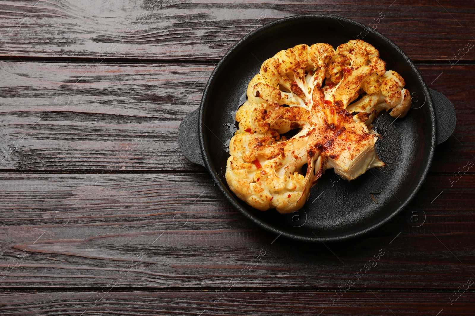 Photo of Tasty cauliflower steak in frying pan on wooden table, top view. Space for text