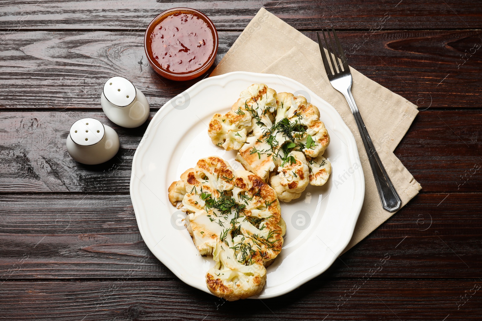 Photo of Delicious grilled cauliflower steaks with sauce and spices on wooden table, flat lay