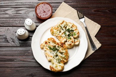 Photo of Delicious grilled cauliflower steaks with sauce and spices on wooden table, flat lay