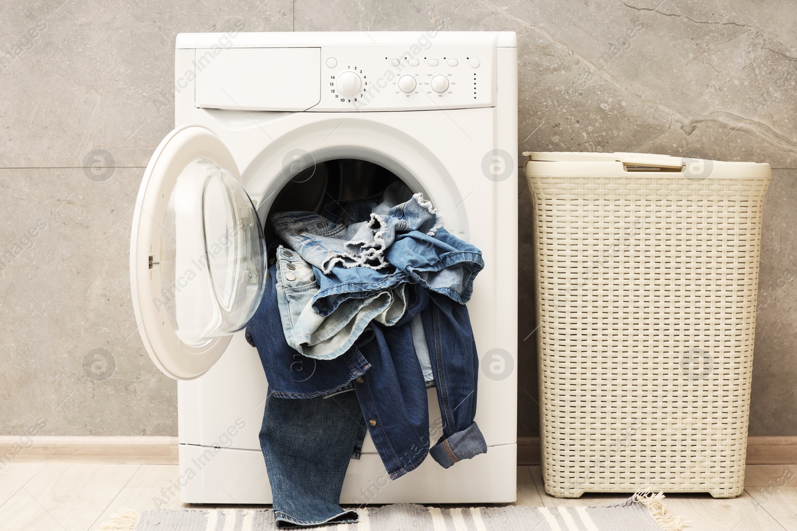 Photo of Washing machine with dirty jeans and other denim clothes indoors