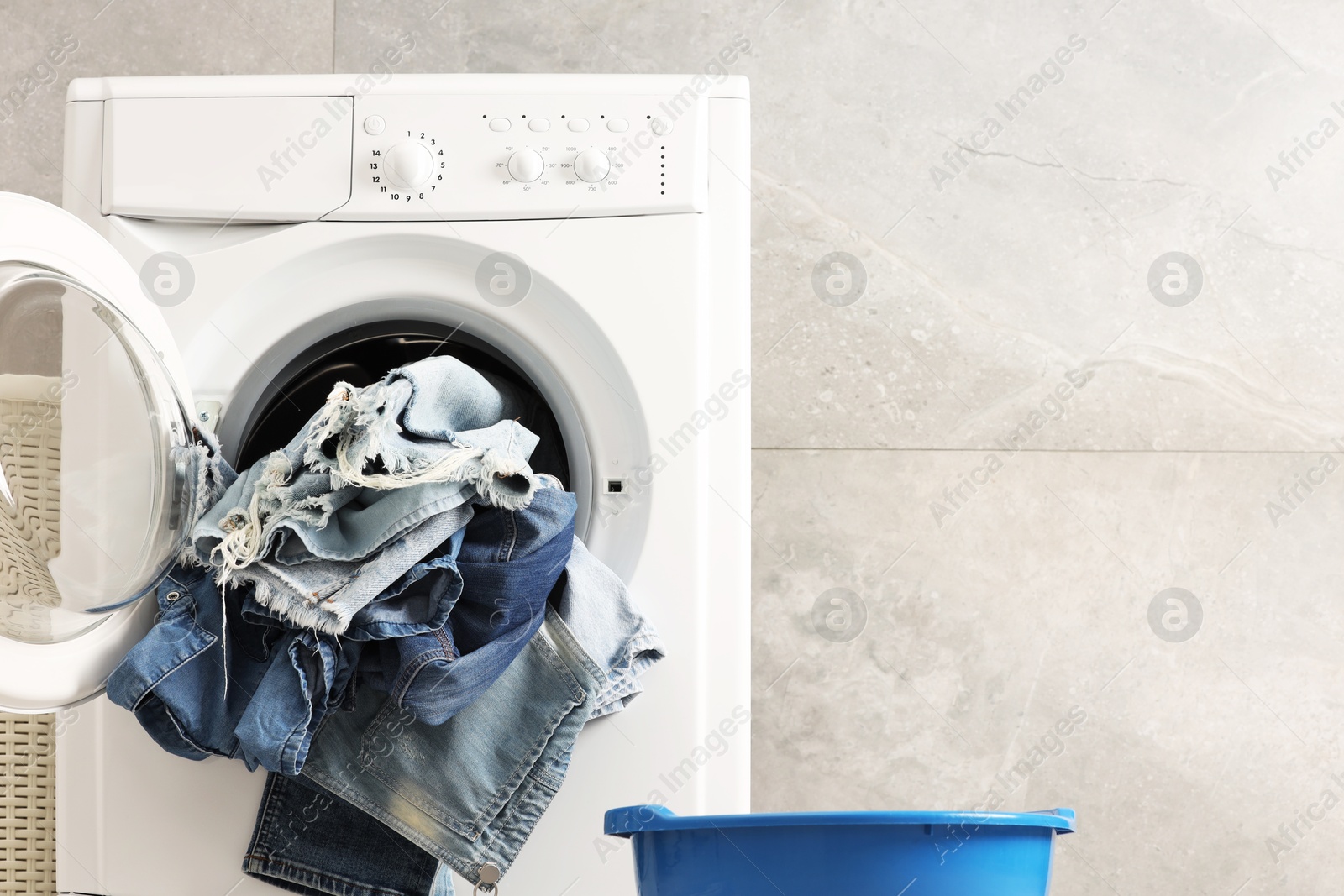 Photo of Washing machine with dirty jeans and other denim clothes indoors, space for text