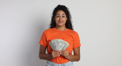 Smiling woman with dollar banknotes on light grey background