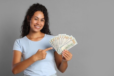 Happy woman with dollar banknotes on grey background, space for text