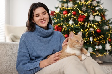 Photo of Woman with cute ginger cat in room decorated for Christmas, selective focus