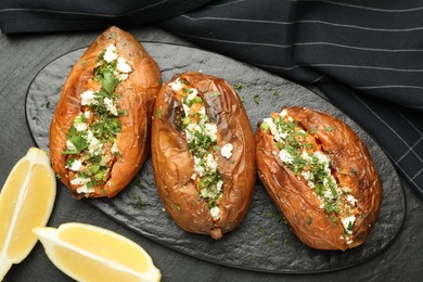 Photo of Tasty baked sweet potatoes with feta cheese, parsley and lemon slices on dark textured table, flat lay