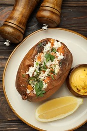 Photo of Tasty baked sweet potato with feta cheese, parsley, sauce, lemon slice and spices on wooden table, flat lay