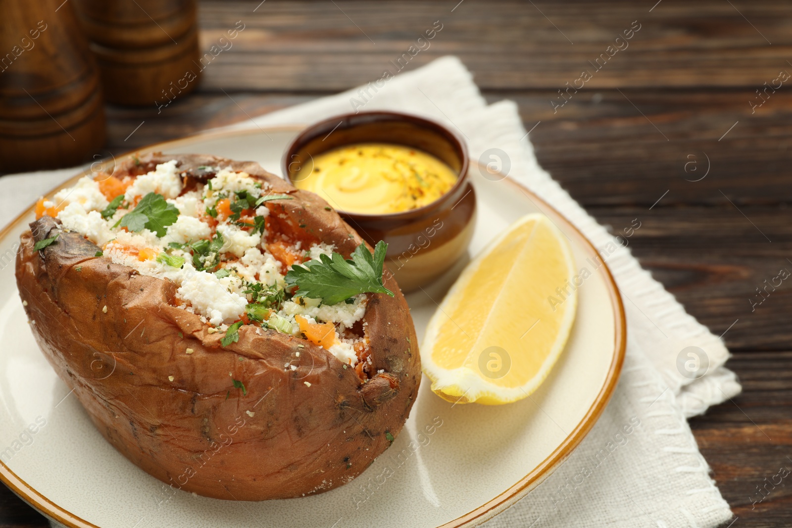 Photo of Tasty baked sweet potato with feta cheese, parsley, sauce and lemon slice on wooden table, closeup