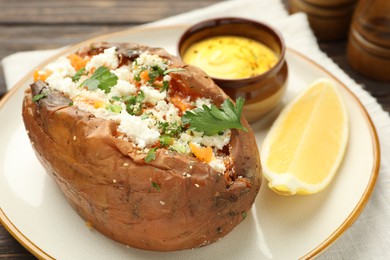 Photo of Tasty baked sweet potato with feta cheese, parsley, sauce and lemon slice on table, closeup