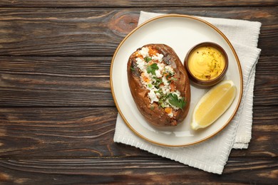 Tasty baked sweet potato with feta cheese, parsley, sauce and lemon slice on wooden table, top view. Space for text