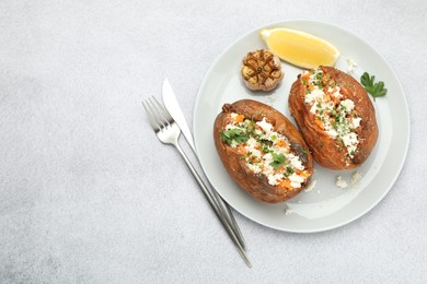 Tasty baked sweet potatoes with feta cheese, parsley, garlic and lemon slice on light textured table, top view. Space for text