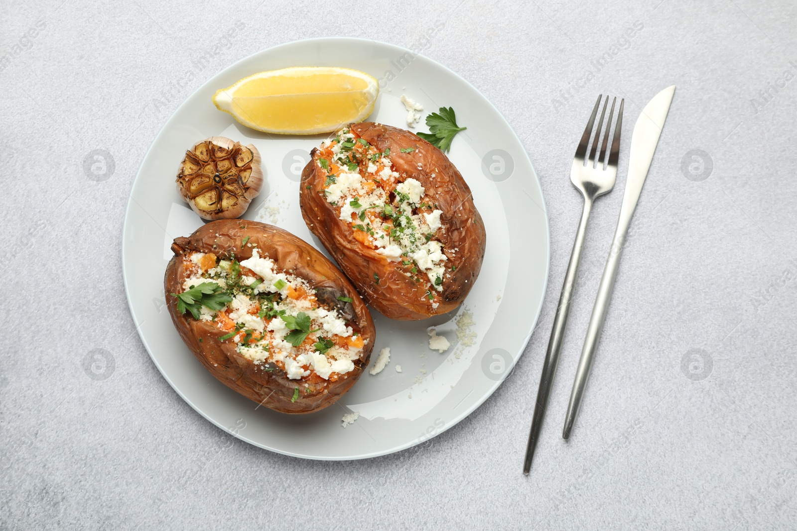 Photo of Tasty baked sweet potatoes with feta cheese, parsley, garlic and lemon slice on light textured table, top view