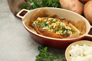 Photo of Tasty baked sweet potato with feta cheese and herbs on grey textured table, closeup