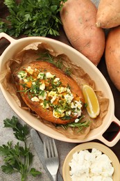 Photo of Tasty baked sweet potato with feta cheese and herbs on grey textured table, flat lay