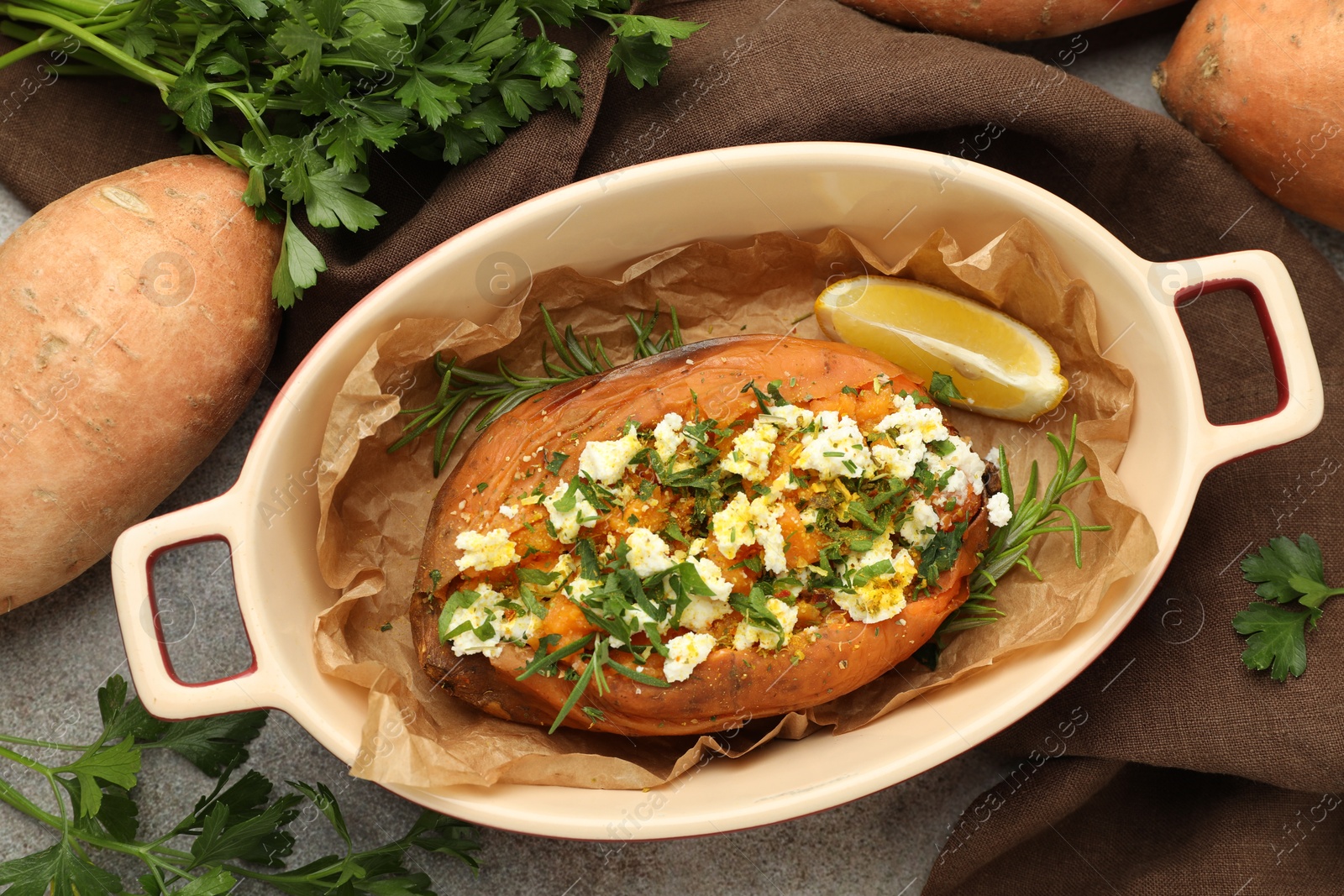 Photo of Tasty baked sweet potato with feta cheese and herbs on grey textured table, flat lay