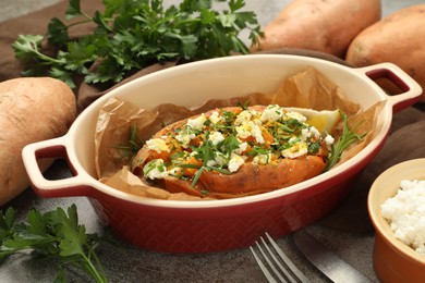 Photo of Tasty baked sweet potato with feta cheese and herbs on grey textured table, closeup